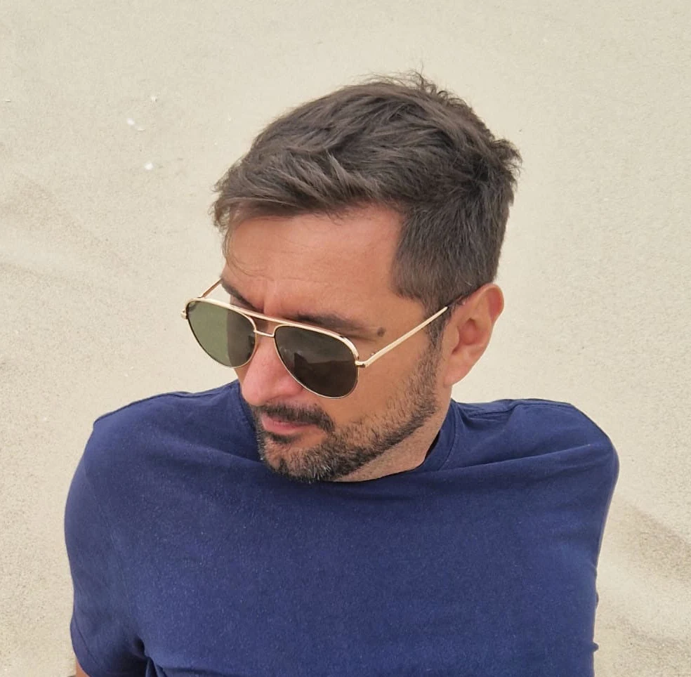 Paweł Czebreszuk seated on sand, wearing sunglasses and a navy shirt